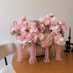 Pink floral arrangement in a textured bowl with cascading bead strands