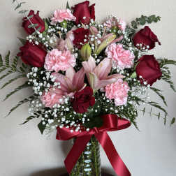 Bouquet of red roses and pink carnations in a glass vase with a red ribbon