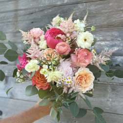 Handheld bouquet of pink, peach, and cream flowers with greenery