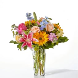 Mixed bouquet of roses, lilies, and sunflowers in a clear glass vase