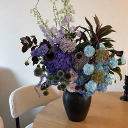 Tall mixed bouquet in a black vase with blue, purple, and white flowers
