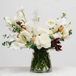 White floral arrangement in a clear glass vase with calla lilies and ranunculus