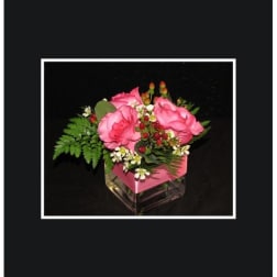 Pink roses arranged in a square glass vase with greenery