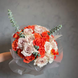 Bouquet of coral, blush, and white roses with eucalyptus in translucent wrap