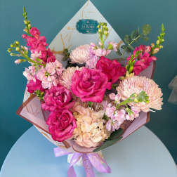 Pink roses and pale chrysanthemums in a wrapped bouquet with a lavender ribbon
