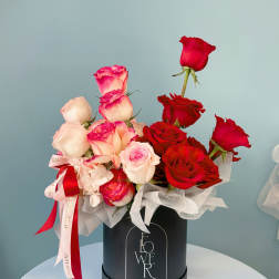 Red and blush roses arranged in a black hat box with ribbon