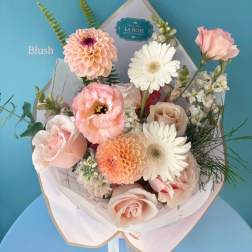 Blush bouquet with roses, gerbera daisies, and peach blooms in white wrap