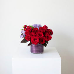 Red roses and lavender flowers in a purple glass vase