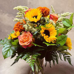 Bouquet of sunflowers, roses, and orange carnations in a glass vase