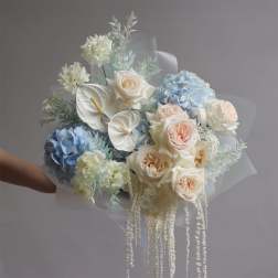 Bouquet of blue hydrangeas, cream roses, and white anthuriums with trailing white accents
