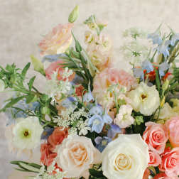 Pastel bouquet of roses, blue flowers, and white blooms in a white vase