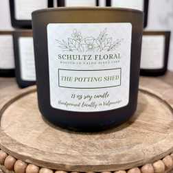 Black jar candle labeled "The Potting Shed" on a wooden tray