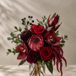 Deep red bouquet in a clear glass vase with roses and tropical blooms