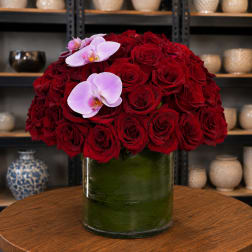 Red rose arrangement in a glass vase with two pale pink orchids