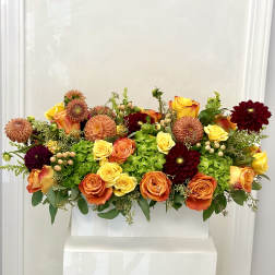 Mixed bouquet of orange, yellow, and burgundy flowers in a white container