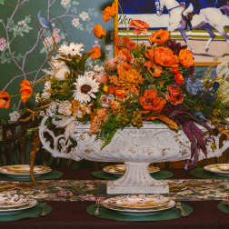 Large orange and white floral centerpiece in an ornate white urn on a dining table