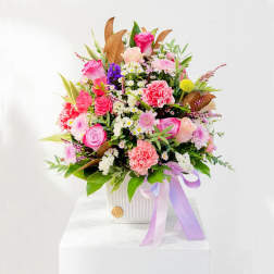 Mixed pink and white flower arrangement in a white vase with a lavender ribbon