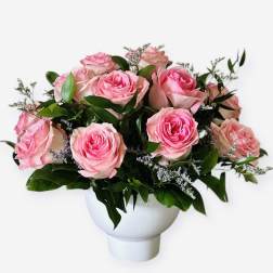 Pink roses arranged in a white vase with greenery