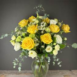 Yellow and white roses in a clear glass vase with airy filler flowers