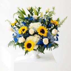 Large bouquet of sunflowers, white roses, and blue flowers in a white vase