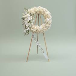 White floral wreath on a wooden easel with condolence ribbons