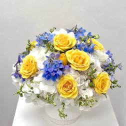Yellow roses and blue flowers arranged in a white vase