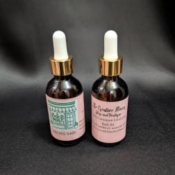 Two dropper bottles of body oil with pink labels on a dark background