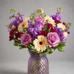 Purple and pink bouquet with cream daisies in a textured glass vase