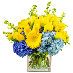 Yellow roses and calla lilies with blue hydrangeas in a glass vase
