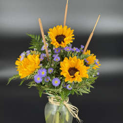 Sunflowers and purple daisies in a glass vase with raffia tie