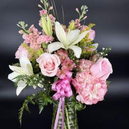 Pink roses and lilies arranged in a glass vase with a pink ribbon