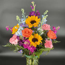 Colorful mixed bouquet in a clear glass vase with sunflowers, roses, and carnations