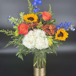Mixed bouquet with sunflowers, roses, blue delphinium, and white hydrangea in a glass vase