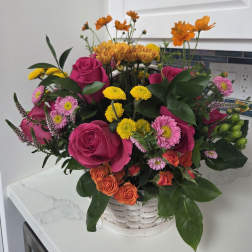 Mixed bouquet of pink roses, yellow mums, and orange flowers in a white basket