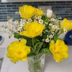 Yellow tulips and white daisies in a clear glass vase