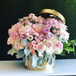 Pink and white roses arranged in a gold hatbox with pearl strands