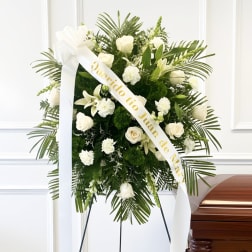 White funeral wreath with ribbon on an easel beside a casket
