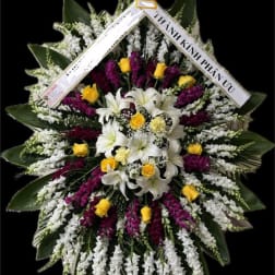 Large standing floral wreath with white lilies, yellow roses, and purple flowers