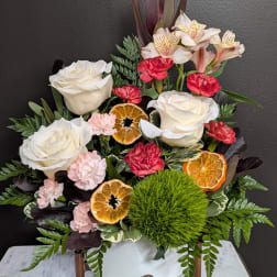White roses and pink carnations arranged with dried orange slices in a vase
