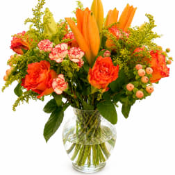 Orange lilies and roses in a clear glass vase