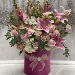Pink and white floral arrangement in a magenta hat box with a ribbon bow