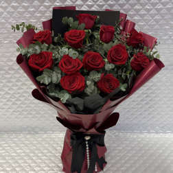 Bouquet of red roses wrapped in burgundy paper with a black ribbon
