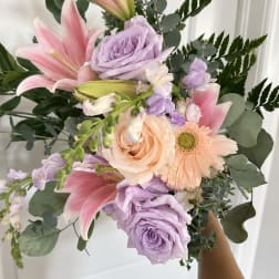 Handheld bouquet of pink lilies, lavender roses, and peach gerbera daisies