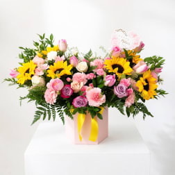 Mixed bouquet with sunflowers, roses, tulips, and carnations in a pink box