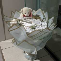 White teddy bear atop a wrapped bouquet of white rolled items