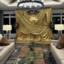 Gold draped event backdrop with floral sprays and a neon Happy Anniversary sign