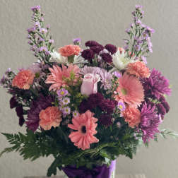 Mixed pink and purple bouquet in a glass vase with a purple ribbon