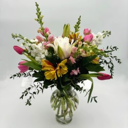 Mixed bouquet of tulips, lilies, and white blooms in a glass vase