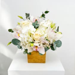 White floral arrangement in a square wooden vase with eucalyptus accents