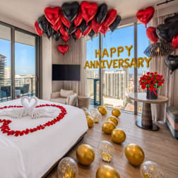 Anniversary room setup with heart balloons, rose petals, and a red rose bouquet